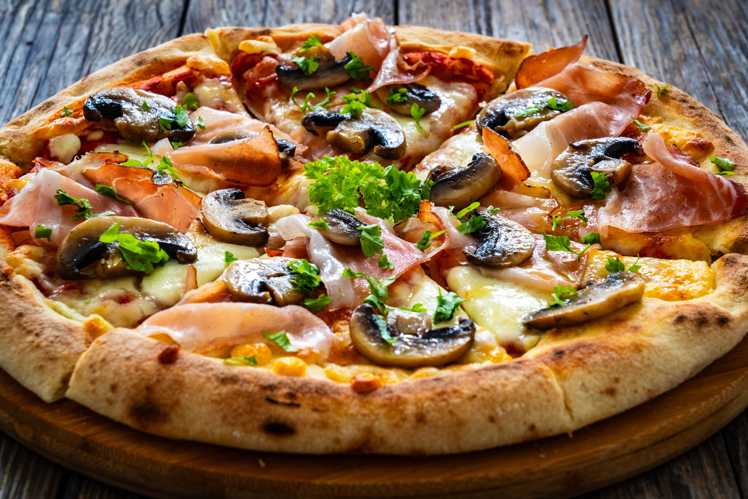 Pizza speck with ham, mozzarella cheese and white mushrooms on wooden background