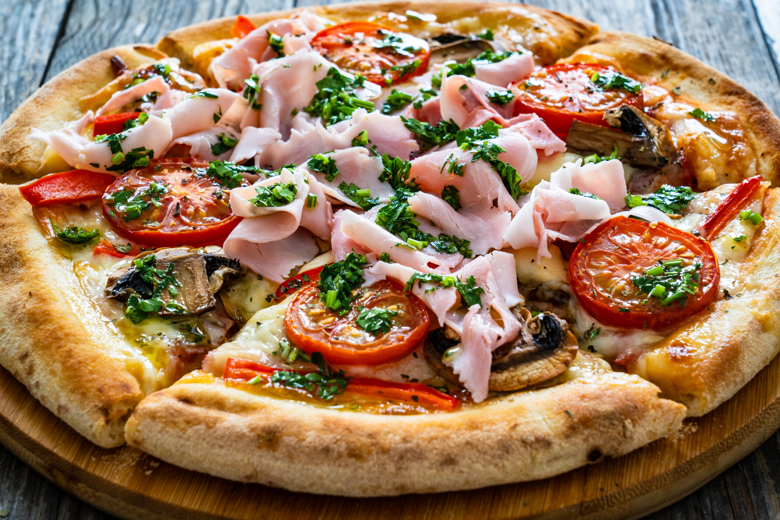 Pizza with ham, mozzarella cheese, sliced tomatoes and white mushrooms on wooden background